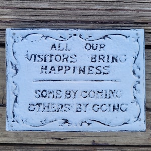 May include: White sign with black lettering that reads "All our visitors bring happiness, some by coming, others by going."