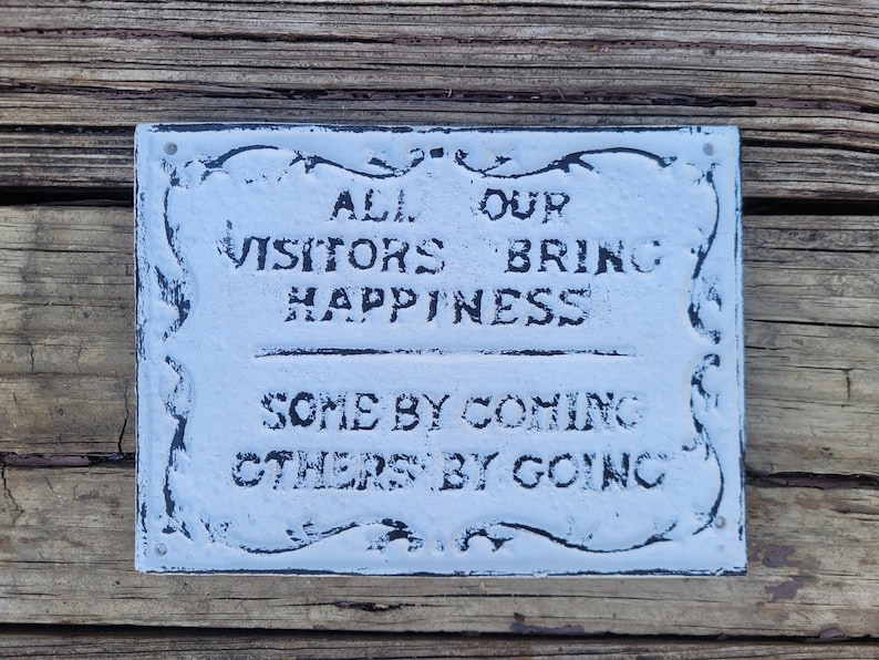 May include: White sign with black lettering that reads "All our visitors bring happiness, some by coming, others by going."