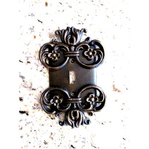 May include: A decorative light switch cover with an ornate, antique-style design. The cover is made of metal and has a dark bronze finish.