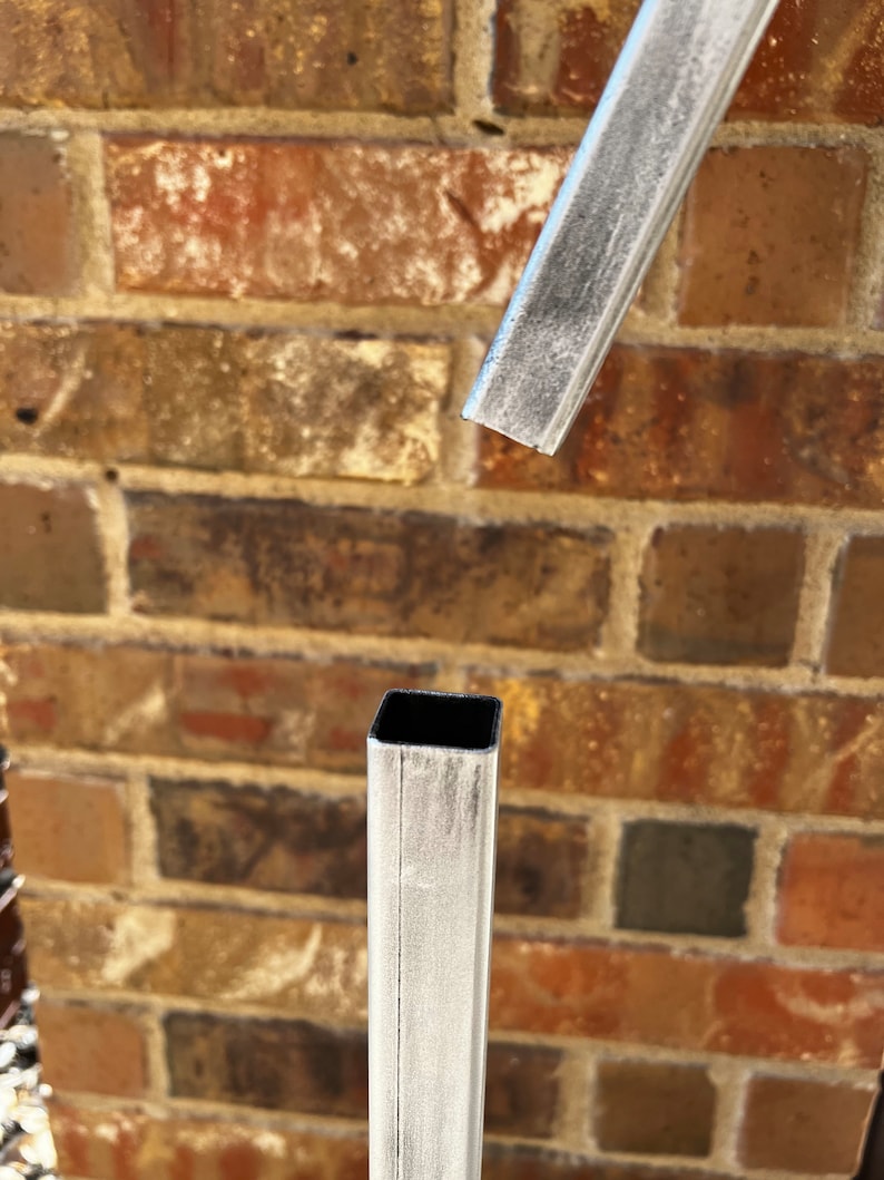 May include: Close-up of two pieces of metal pipe, one is cut and the other is whole. Both are painted white with a textured finish.