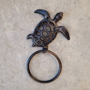 May include: A black cast iron towel ring shaped like a turtle. The turtle has a detailed design and is a decorative accent for a bathroom.