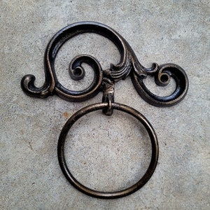 May include: A decorative cast iron towel ring with a scrolled design. The ring is black with a bronze finish.