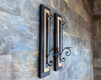 Puede incluir: Un par de candelabros de pared negros con moldura de madera. Cada candelabro tiene un solo brazo de vela con un diseño decorativo de volutas.