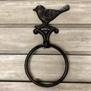 May include: A black metal towel ring with a bird design. The ring is mounted on a wooden wall.