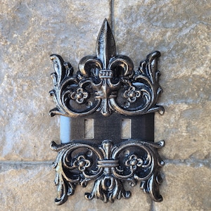 May include: Black cast iron double light switch cover with a fleur-de-lis design.