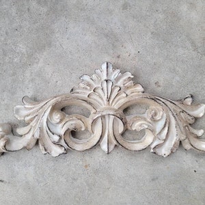 May include: A white, ornate, decorative wall accent with a scroll design. The accent has a distressed, aged look.