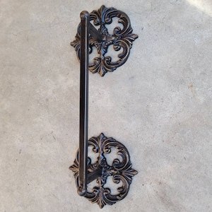 May include: Black metal towel rack with ornate scrollwork on the ends. The rack is mounted to a wall.