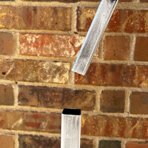 May include: Close-up of a silver metal stand with a square base and a rectangular top. The stand is made of metal tubing and has a brushed finish.