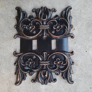 May include: A black and copper double light switch cover with an ornate, decorative design.