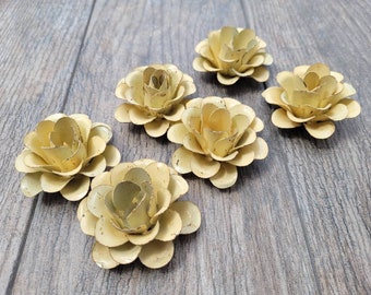 Puede incluir: Seis flores de metal de color amarillo pálido con un acabado desgastado. Las flores están dispuestas sobre una superficie de madera.