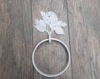 May include: White metal towel ring with a decorative rose design. The ring is attached to a wall.
