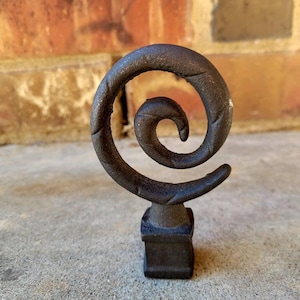 May include: A black metal finial with a spiral design. The finial is on a square base.