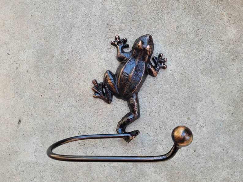 May include: A black metal frog figurine with a bronze finish, holding a black metal toilet paper holder with a round knob.