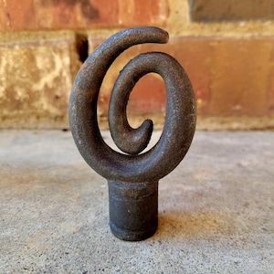 Może przedstawiać: Czarny metalowy zwieńczenie ze spiralnym wzorem. Zwieńczenie ma około 12,5 cm wysokości i średnicę około 5 cm.