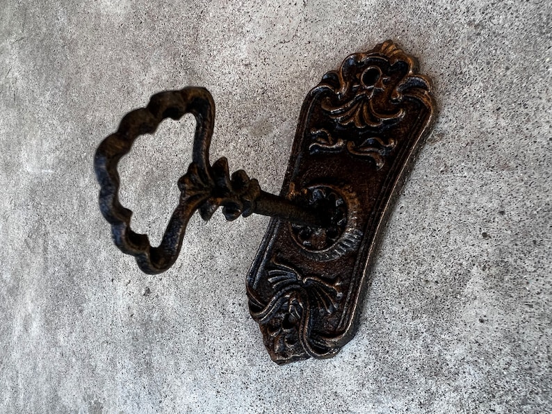 Op de afbeelding: Ouderwetse sleutel en rozet in bronskleurige afwerking. De sleutel heeft een decoratieve handgreep en de rozet heeft gedetailleerde bloemen en krullen. Een vintage-ge&iuml;nspireerd decoratief element.