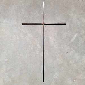 May include: A simple metal cross made of two pieces of metal welded together. The cross is against a plain gray background.