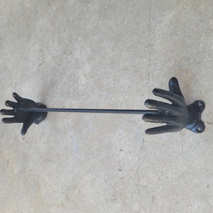 Puede incluir: Toallero de metal negro con dos extremos en forma de mano. El toallero está montado en una pared.