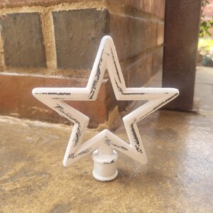 May include: White metal star finial with a distressed finish. The star has a hollow center and a round base.