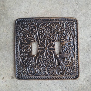 May include: A decorative double light switch cover with an ornate, embossed floral design in a dark bronze finish.