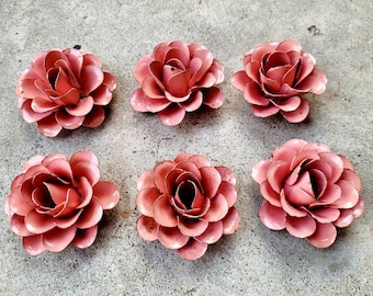 Puede incluir: Seis decoraciones florales antiguas de metal en color rosa empolvado. Las flores tienen múltiples capas de pétalos y están dispuestas sobre una superficie de hormigón. Estas flores son probablemente para la decoración del hogar o proyectos de manualidades.