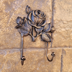 May include: A cast iron wall hook with a decorative rose design. The hook has two hooks, one on each side of the rose.