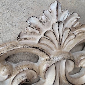 May include: A white, ornate, decorative piece with a distressed finish. The piece has a floral design with intricate details. It is made of a durable material and is perfect for adding a touch of elegance to any room.