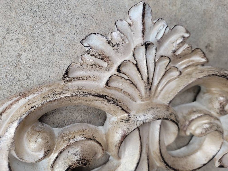 May include: A white, ornate, decorative piece with a distressed finish. The piece has a floral design with intricate details. It is made of a durable material and is perfect for adding a touch of elegance to any room.