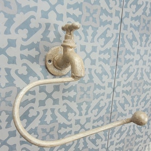 May include: A gold-colored metal toilet paper holder shaped like a faucet with a decorative, patterned background.