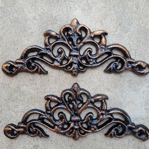 May include: Two ornate metal decorative pieces in a bronze finish. Each piece is shaped like a crown with intricate scrollwork and a floral design.