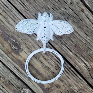 May include: White cast iron bee towel ring with a distressed finish. The bee has wings and a ring for hanging towels.