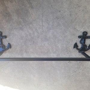 Puede incluir: Barra toallero de metal negro con extremos en forma de ancla. La barra está montada en una pared gris.