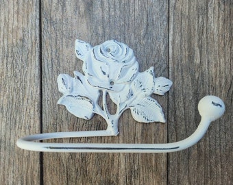May include: White cast iron toilet paper holder with a rose design. The holder features a decorative scroll design and a round knob.