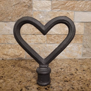 May include: A black metal heart-shaped finial with a decorative design. The finial is made of cast iron and has a smooth, polished finish.