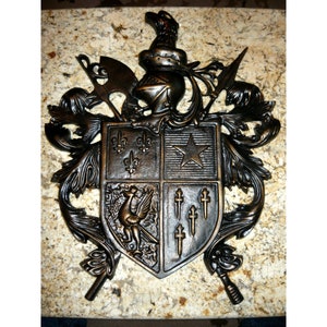 May include: A bronze metal coat of arms with a shield, helmet, and other heraldic symbols. The shield is divided into four sections, each with a different design. The top left section features three fleurs-de-lis, the top right section features a five-pointed star, the bottom left section features a bird, and the bottom right section features five crosses.