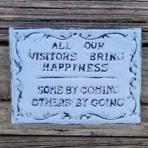 May include: White metal sign with black lettering that reads "All our visitors bring happiness, some by coming others by going."