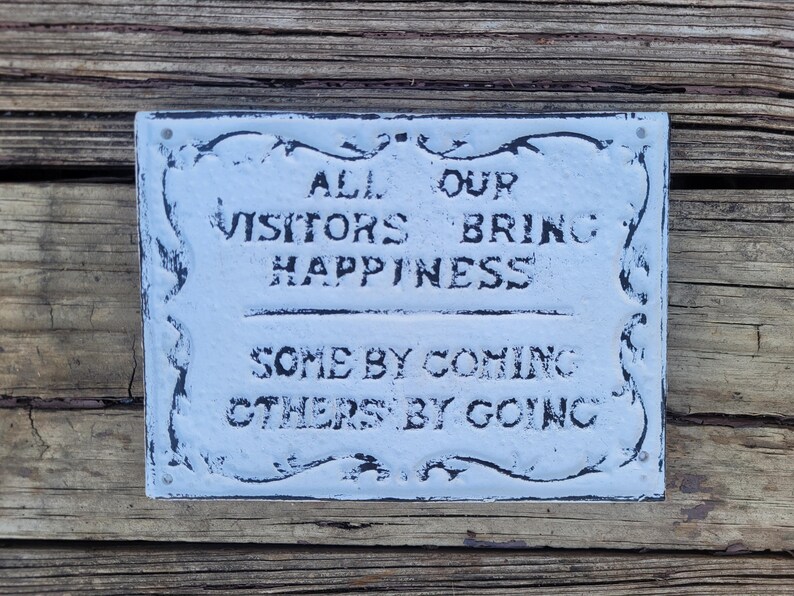 May include: White metal sign with black lettering that reads "All our visitors bring happiness, some by coming others by going."