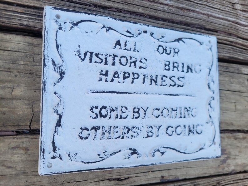 May include: White metal sign with black lettering that reads "All our visitors bring happiness, some by coming, others by going."