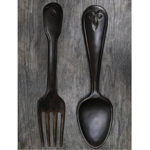 May include: A black metal fork and spoon wall decor. The fork has a decorative design at the top and the spoon has an owl design.