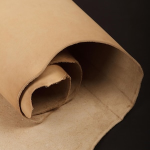 May include: A close-up of a rolled piece of light brown leather. The leather is smooth and has a natural grain.