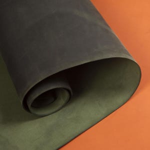 May include: A rolled-up piece of dark green leather, revealing a lighter green underside. The leather has a matte finish and is set against an orange background.