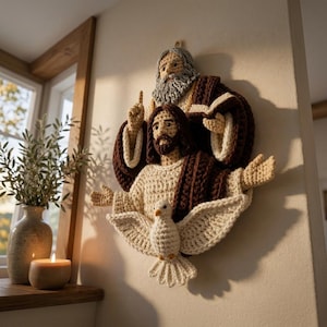 Könnte beinhalten: Ein gehäkeltes Wandbild, das eine religiöse Szene mit drei Figuren darstellt. Die obere Figur hat einen grauen Bart, die mittlere einen braunen Bart und eine erhobene Hand, und eine weiße Taube mit ausgebreiteten Flügeln befindet sich unten.