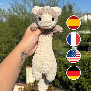 May include: A plush, crocheted ferret toy made from soft, textured yarn. The ferret features a cream-coloured body and tail with light brown markings on its head and ears, small black safety eyes, and a tiny pink embroidered nose.
