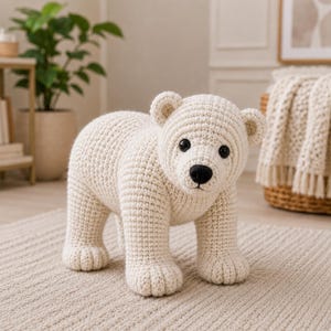 May include: A cream-colored crocheted polar bear figurine featuring a textured yarn surface, two round black eyes, and a small black nose. The bear is standing on all four legs with rounded paws and small, circular ears on its head.
