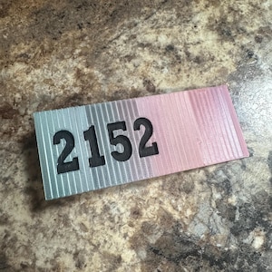 May include: A close-up of a light blue and pink rectangular tag with the number 2152 printed in black.