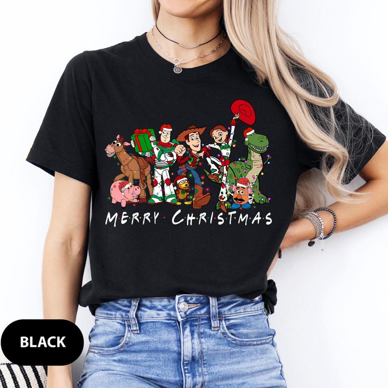 May include: Black t-shirt featuring a graphic of Toy Story characters with Christmas decorations and the text "MERRY CHRISTMAS". The design includes Woody, Buzz Lightyear, and other characters. A festive holiday tee.