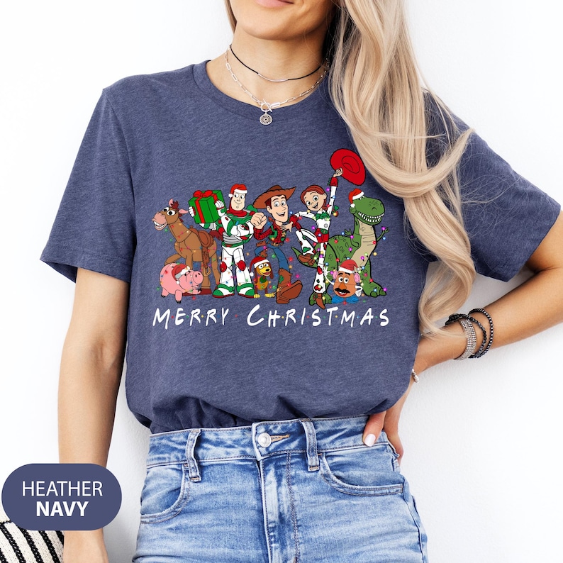 May include: Heather navy blue t-shirt featuring a graphic of Toy Story characters in Christmas attire. The design includes Woody, Buzz Lightyear, and others, with the text "MERRY CHRISTMAS" in white.