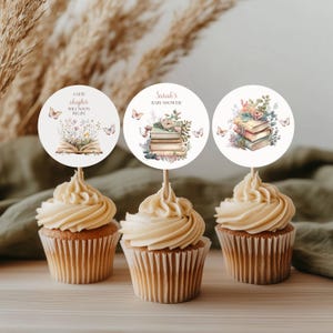 Puede incluir: Tres cupcakes con glaseado blanco cubiertos con adornos redondos de papel para cupcakes que representan una pila de libros, flores y mariposas. El texto en los adornos dice "Un nuevo capítulo pronto comenzará" y "Baby Shower de Sarah".