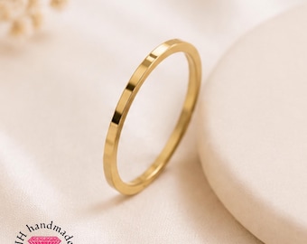 Puede incluir: Un anillo de banda de oro pulido fino con una superficie lisa y plana. El anillo está colocado en ángulo, mostrando su diseño circular simple. El logotipo JH handmade jewellery con un icono de diamante rosa es visible abajo.