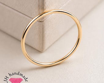 Puede incluir: Un anillo de oro fino y pulido con una banda circular lisa. La joya está colocada frente a una superficie texturizada de color claro. La esquina inferior izquierda presenta el texto JH handmade jewellery con un icono de diamante rosa.