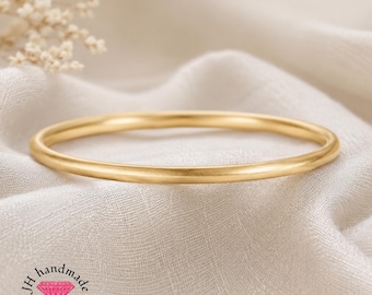 Puede incluir: Una pulsera tipo brazalete circular de oro con un acabado pulido y liso. La pieza de joyería se presenta sobre una tela blanca de textura suave. La imagen incluye un logotipo con el texto JH handmade jewellery y un icono de diamante rosa.